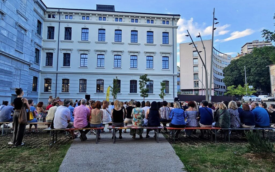 Ljudi koji sjede na klupama ispred Gradske knjižnice Rijeka, u Art-kvartu Benčić.